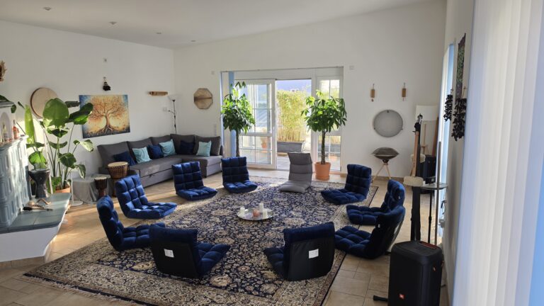 Großzügiger, heller Seminarraum der Praxis Schonfeld mit gemütlicher Sofaecke, blauen Bodenstühlen im Kreis und Blick auf die Terrasse – ideal für Gruppenarbeit und Entspannung.