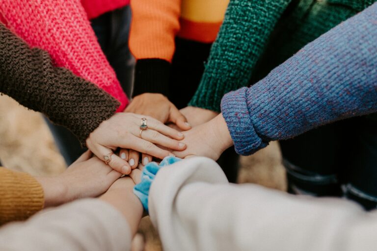 Mehrere Hände liegen als Zeichen für Zusammenhalt, Gemeinschaft und Gruppentherapie aufeinander.